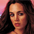 Pixelated close-up of a person with long dark brown hair, light skin, and red lips against a pinkish background.