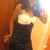 A person in a black strapless dress poses with one arm raised against an orange background.