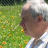 Pixelated image of a person with light skin tone and short dark hair, wearing white clothing against green grassy background.