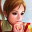 Pixelated static image of a person with short brown hair wearing a green top, holding an object with red and yellow colors against a light blue background.