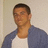Pixelated static image of a person with short dark hair wearing a white shirt under a blue jacket against a light background.