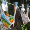 Colorful knitted shoes hang on a clothesline with blue pegs, one showing a rainbow stripe pattern and the other a pink fish design with a blue eye.