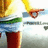A pixelated figure in yellow, white, green, and red clothing with a blurred background showing partial text.
