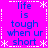 A static image with a bright pink background displays the phrase "life is tough when ur short" in blue text, repeated four times within a white dotted border frame adorned with small snowflake symbols.
