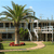 Pixelated static image of a two-story building with dark windows, a palm tree, and a red object on grass under a light blue sky.