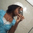 Pixelated image of a person with dark hair wearing a light blue and white top, holding an object near their face against a gradient background.
