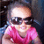 Pixelated image of a person wearing dark sunglasses and a pink top against a dark background with blue and white highlights.