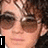 A pixelated image of a person with curly brown hair and sunglasses, featuring text overlays in black boxes.