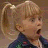Pixelated image of a blonde girl with pigtails shouting text on a brown background.