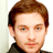 Static pixelated image of a person's head and shoulders with brown hair, light skin tone, and dark clothing against a plain background.