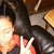 A pixelated image shows a person with dark hair and light skin wearing a red top, positioned against a blurred background of warm tones.