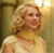 Static pixelated image of a woman with curly blonde hair wearing a light-colored sleeveless top against a warm-toned background.