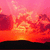 A sunset scene with pink and orange clouds over a dark silhouette of land, transitioning from solid to partially obscured.