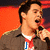 A person holding a microphone against an orange background with blue text overlays showing different letter sequences.