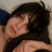 A pixelated close-up of a person with dark hair lying down, showing part of their face and shoulder against a light background.