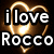 Animated icon with glowing golden hearts and white text reading "i love Rocco" on the left, transitioning to "with all my heart" on the right.