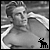 Black-and-white pixelated image of a shirtless person with short hair, arms raised in motion, featuring a small animal icon at the bottom right.