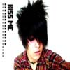 A person with spiky black hair wearing a red and brown plaid shirt, with vertical text reading "KISS ME" on the left side of the image.
