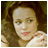 Pixelated close-up of a person with light skin, brown hair, and pink lips wearing a white top against a dark background.