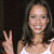 A pixelated static image shows a person with long dark hair wearing a white sleeveless top, making a peace sign with their right hand against a dark background.