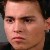 Pixelated close-up of a person's face with light skin tone, dark hair, and neutral expression against dark background.