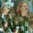 Two pixelated figures with light brown hair and green tops stand side-by-side against a blurred background.