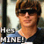 A person with brown hair and sunglasses wears a blue shirt, standing in front of a blurred background with text reading "Hey MINE!" on the left side.