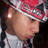 Pixelated close-up of a person wearing red and white striped headwear, light-colored clothing, with visible ear and partial facial features.