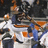 Pixelated static image of two figures in dynamic poses with orange, blue, white, and dark gray tones against a dark background.