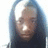 Pixelated static image of a person with light skin tone, dark hair, and neutral expression wearing dark clothing against blurred background.