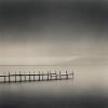 A static image of a wooden pier extending over calm water under a gradient sky transitioning from dark gray to light beige.
