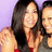 Three people pose together in a pixelated image with light purple background; central figure has long dark hair and red straps, right figure wears gray top.