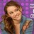 Pixelated image of a person with long brown hair wearing a blue top against a purple background with white square patterns.