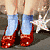 Static pixelated image of a person's lower legs and feet wearing blue socks and red shoes with white accents, standing on a textured surface next to a star-shaped object.