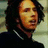 Pixelated static image of a person with dark curly hair wearing a black top and silver necklace against light background.
