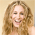 A pixelated close-up of a smiling person with long wavy light brown hair against a plain light background.