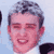 Pixelated static image of a person's face with short dark hair and light skin, wearing a white shirt under a dark jacket against a light blue background.