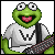 Pixelated green frog character with large eyes and pink mouth, wearing white shirt with black 'W' symbol, holding patterned object against gray background.