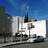 Pixelated static image of a building facade with a blue sky background, featuring a large white sign with partial text and dark structural elements.