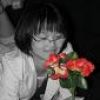 A grayscale figure holding a bouquet of red roses with green leaves, partially obscured by a white garment on the left.