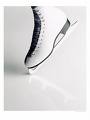 Static close-up of a white ice skate blade on a reflective surface with blurred background elements.