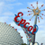 Pixelated image of a red and blue character with a golden crown-like object, set against a light blue sky background.