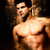 A shirtless man with dark hair stands against a dark background, his torso and arms visible in a muscular pose.