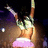 Pixelated figure with arms raised, wearing green top and pink skirt against dark background.