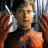 A pixelated contact sheet showing two frames of an animated icon featuring a character in orange and black attire holding a silver object against a metallic background, with green text reading "Original Icons .com" on the right side.