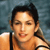Pixelated close-up of a person with short dark hair wearing a sleeveless top against a blurred blue background.