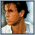 Pixelated close-up of a person with dark hair and light skin wearing a white shirt, set against a blurred background.
