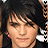 Pixelated close-up of a person with dark hair and light skin, wearing small red earrings against a dark background.