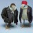 Two pixelated figures in dark coats stand side-by-side against a light blue background, one with brown hair and the other wearing a red head covering.