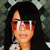 Static pixelated image of a person with long black hair wearing large red-tinted sunglasses and a light-colored top against a dark background.